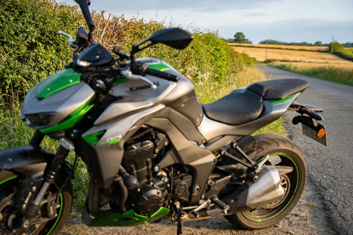 Moto verte et grise stationnée sur une route de campagne, champs et haies en arrière-plan.