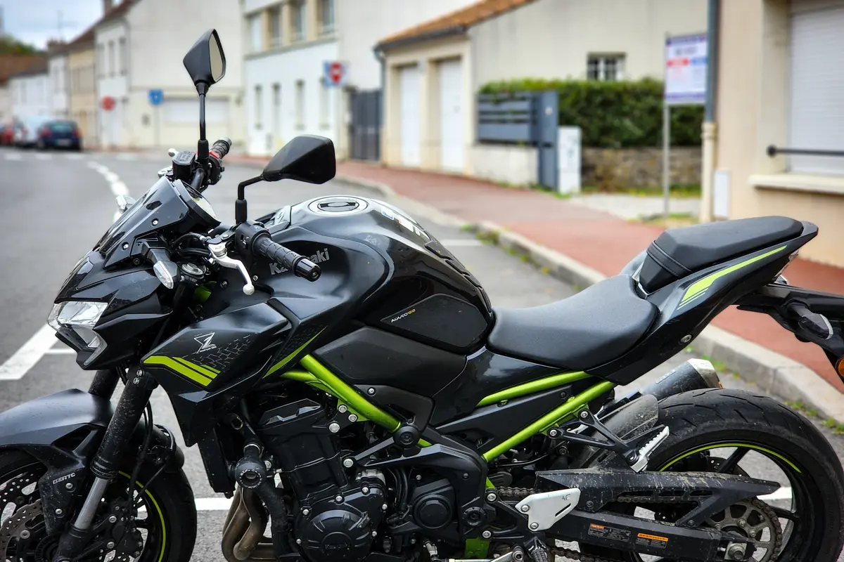 Moto Kawasaki noire et verte garée dans une rue résidentielle, vue de côté. Panneau en arrière-plan.