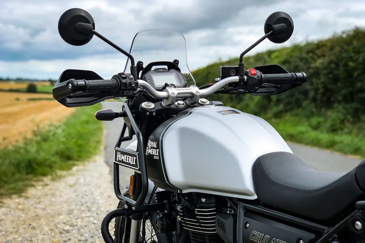 Moto Royal Enfield grise, guidon et rétroviseurs, sur chemin rural, ciel nuageux en arrière-plan.