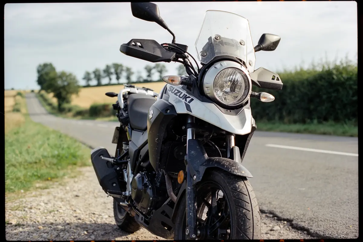 Moto Suzuki stationnée sur une route de campagne, ciel dégagé et arbres en arrière-plan.