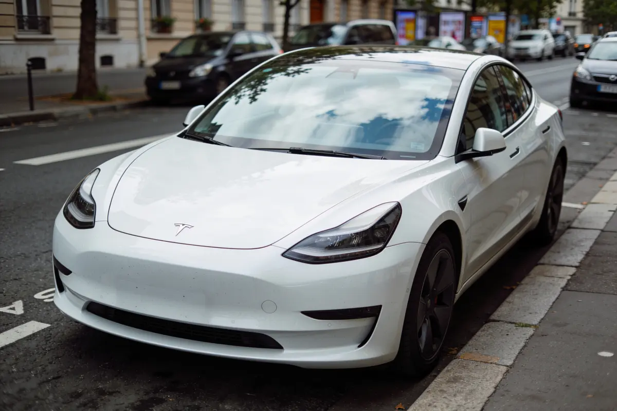 Voiture électrique blanche garée en ville. Modèle de type berline moderne sur rue bordée d’arbres.