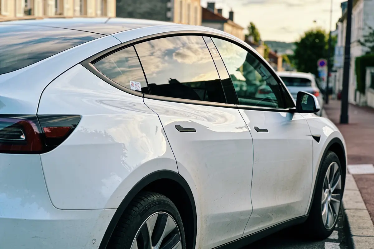Voiture électrique blanche garée en ville, reflet ciel sur vitres.