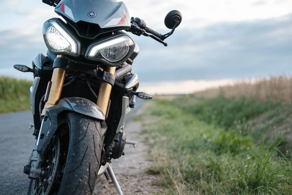 Moto sportive noire stationnée sur une route de campagne, avec ciel nuageux à l'arrière-plan.