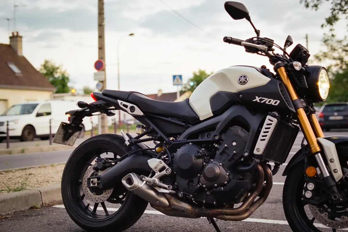 Moto X700 blanche et noire stationnée dans un environnement urbain, avec bâtiments et voitures en arrière-plan.