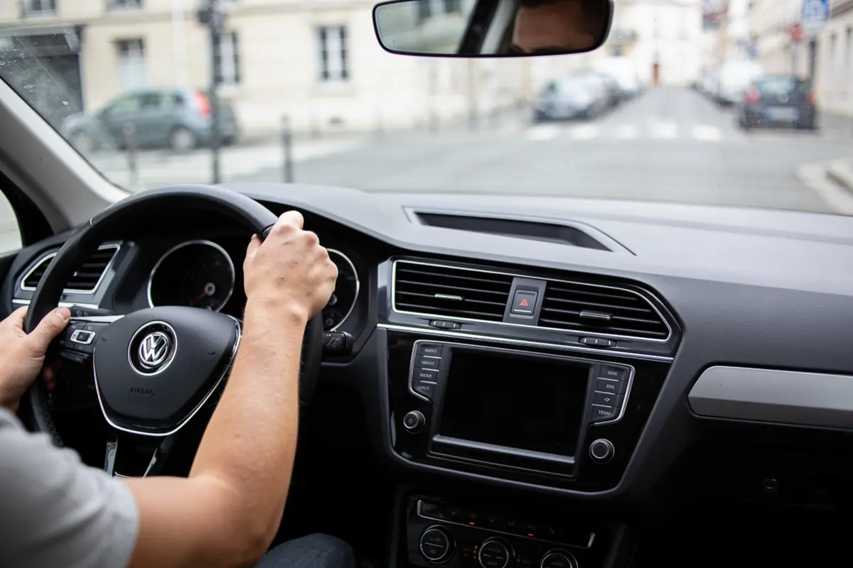 Conducteur tenant le volant d'une voiture Volkswagen sur une rue résidentielle, intérieur bien visible.