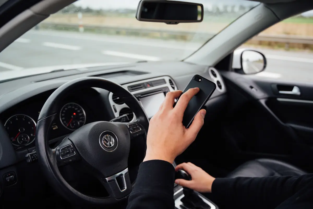 Main tenant un smartphone au volant d'une voiture Volkswagen, intérieur visible.