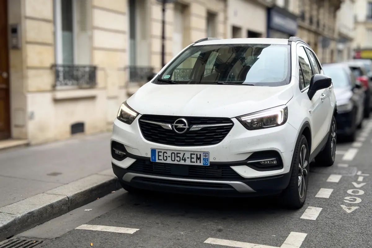 Voiture blanche Opel stationnée dans la rue, devant un immeuble parisien, plaque d'immatriculation visible.
