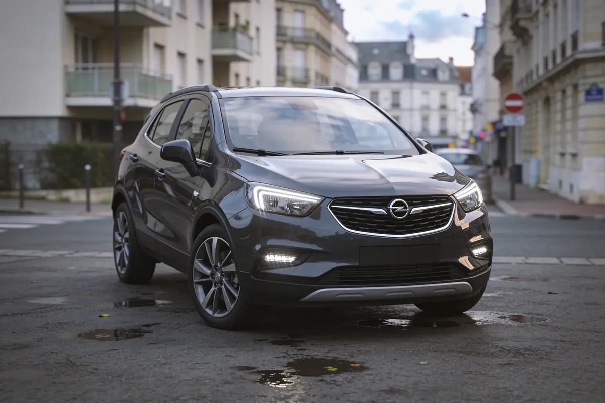 SUV Opel gris stationné dans une rue urbaine, entouré d'immeubles modernes.