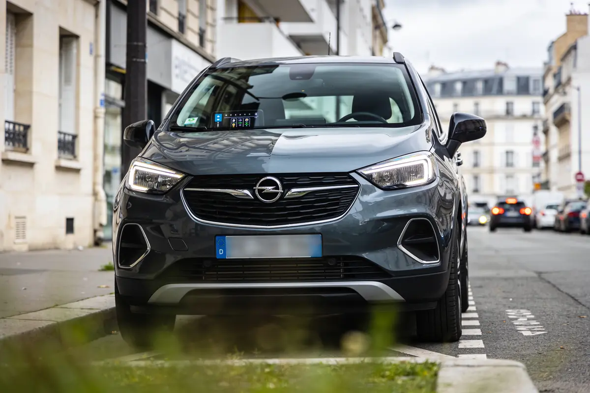 Voiture noire garée dans une rue résidentielle, bâtiments et arbres en arrière-plan.