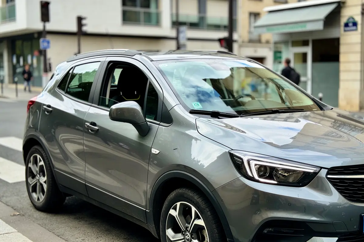Voiture blanche Opel garée dans une rue urbaine avec bâtiments en arrière-plan.