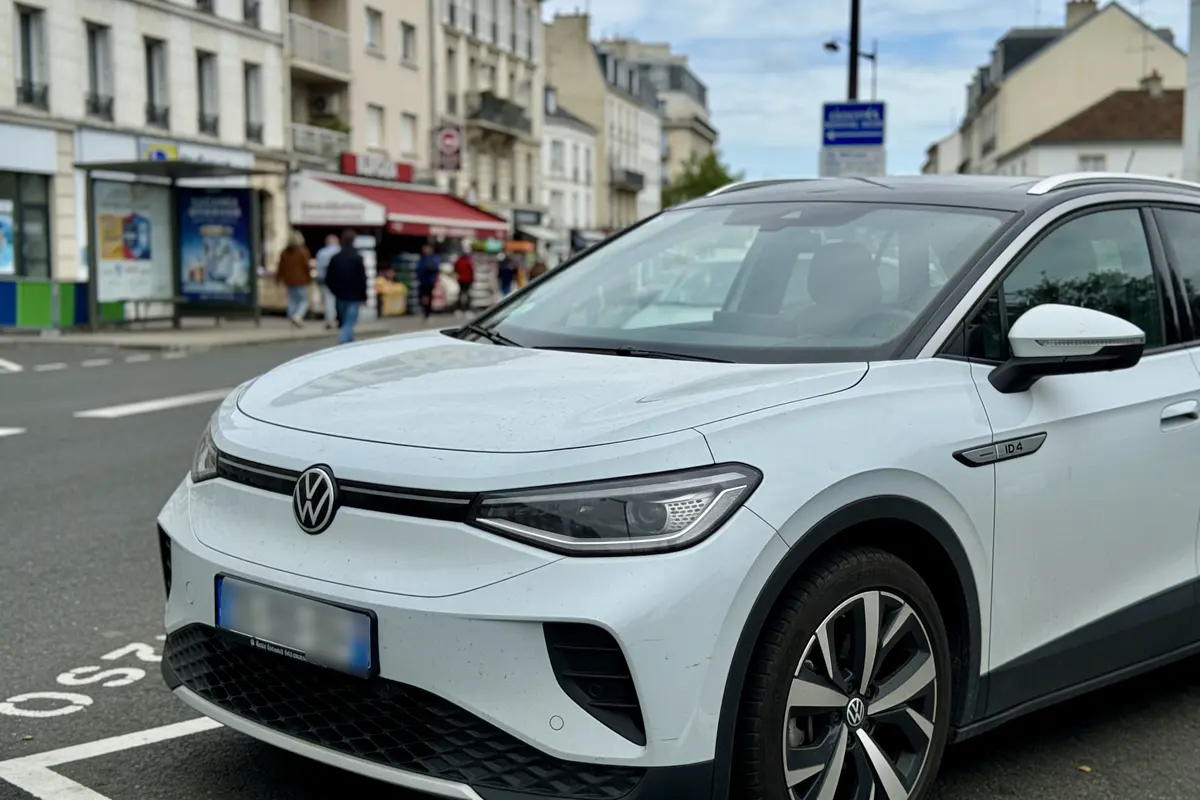 Voiture Volkswagen blanche garée en ville devant des bâtiments et personnes en arrière-plan.